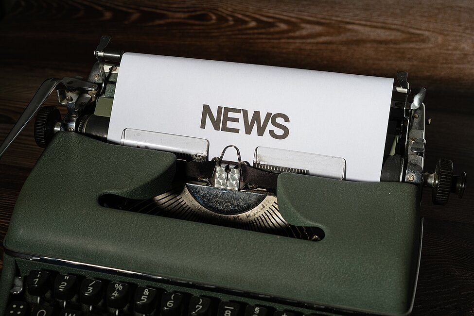 old green typewriter with paper in it where it says "news"