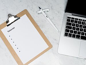 a clipboard with a paper and the word tutorial and bulletpoints on it, a pen, and a piece of a laptop