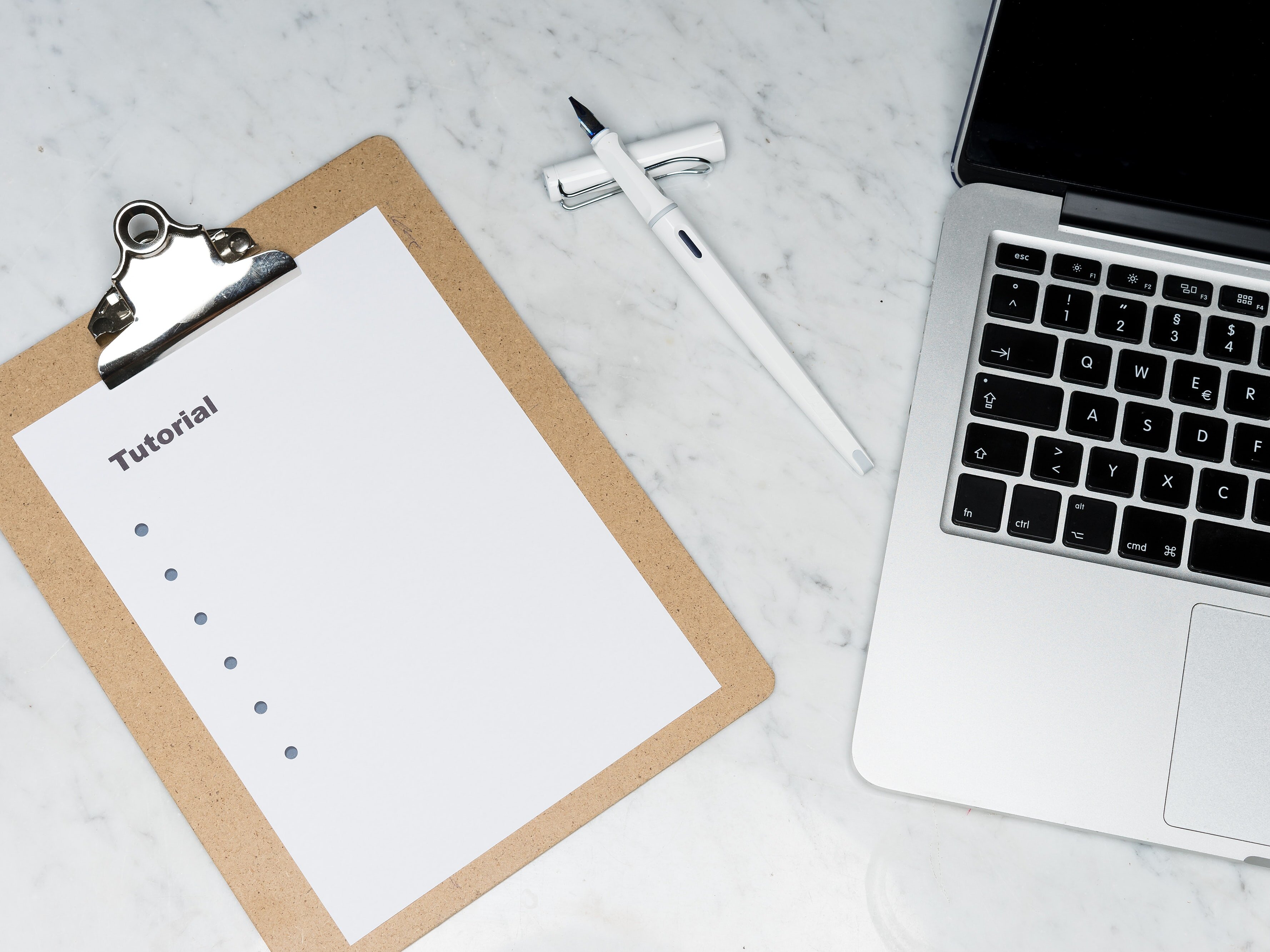 a clipboard with a paper and the word tutorial and bulletpoints on it, a pen, and a piece of a laptop